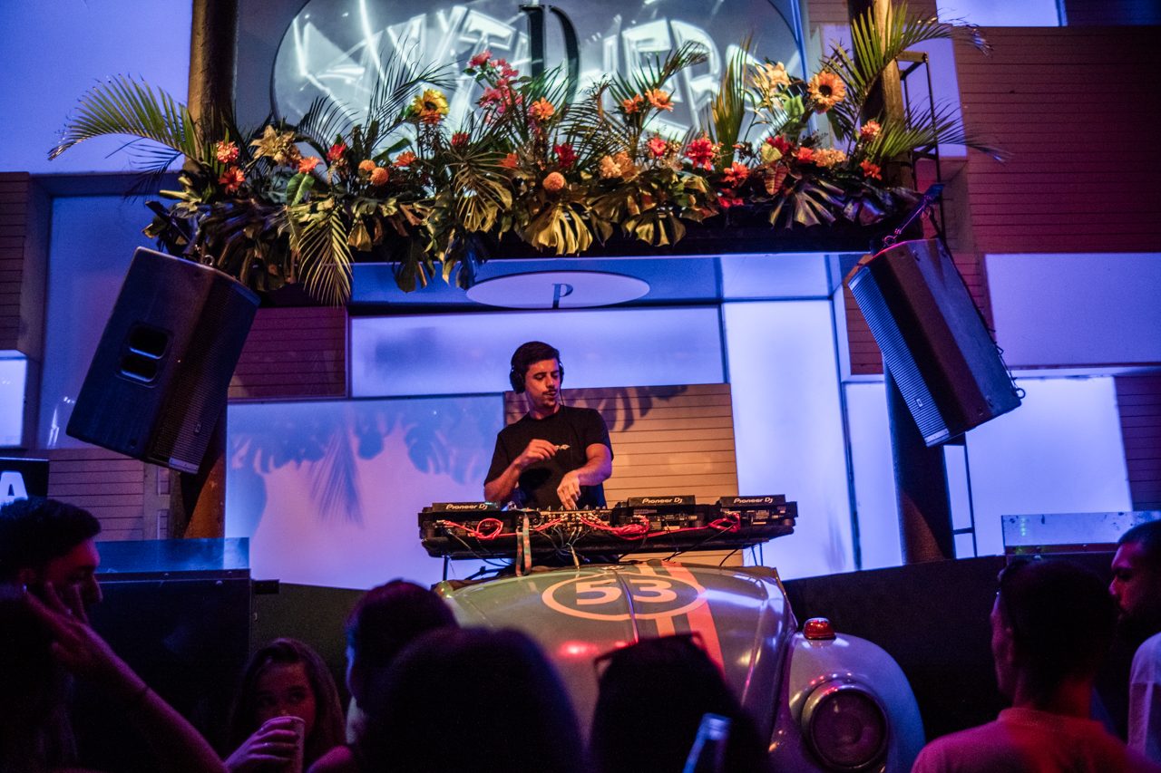 Anti Hero no palco sob o letreiro ANTI HERO, com flores e um Fusca à frente